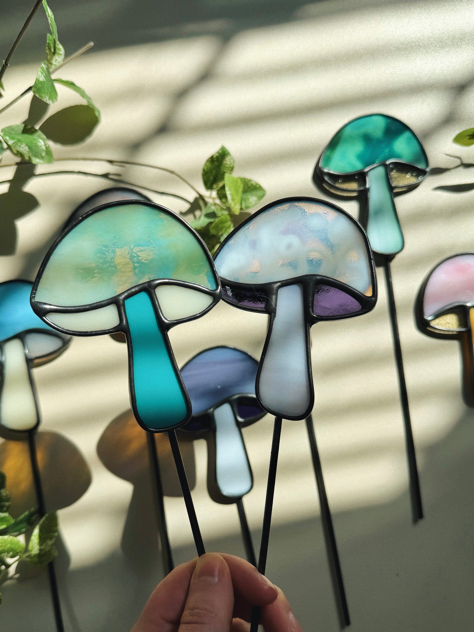 Colorful mushroom-shaped glass on sticks held by a hand with a light background